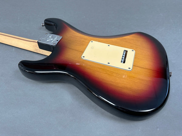 Back view of sunburst finish electric guitar body with maple neck and cream plastic backplate on gray surface