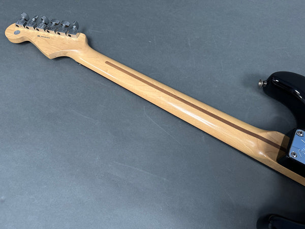 Maple guitar neck with skunk stripe and chrome tuning pegs on black electric guitar shown from the back on gray background