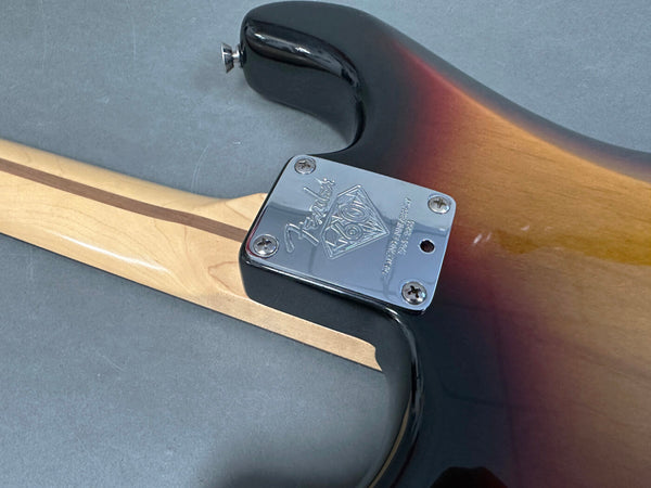 Close-up of Fender 70th Anniversary electric guitar neck plate with screws on sunburst body and maple neck with skunk stripe on gray background