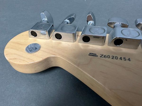 Close-up of Fender guitar headstock back showing chrome tuning pegs, serial number Z6020454, and 60th anniversary badge on natural wood finish