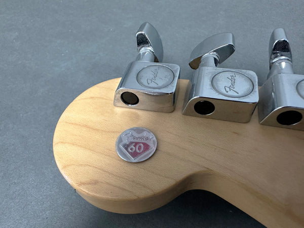 Close-up of Fender guitar headstock with vintage-style tuning pegs and a Fender 60th anniversary badge on natural wood finish