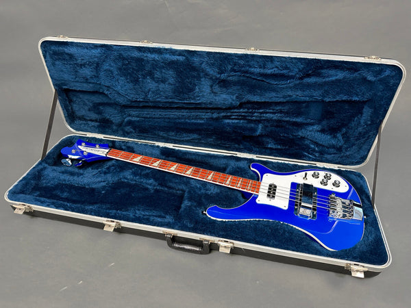 Blue electric bass guitar with white pickguard in hard shell case lined with dark blue plush interior on gray floor