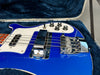 Close-up of blue electric bass guitar body with white pickguard, chrome bridge, and control knobs in a blue plush-lined hard case