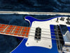Close-up of blue electric bass guitar with white pickguard, chrome bridge cover, and rosewood fretboard inside a plush blue guitar case