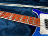 Close-up of bass guitar fretboard with pearl inlays and silver frets on blue body with white pickguard resting on navy blue plush case interior