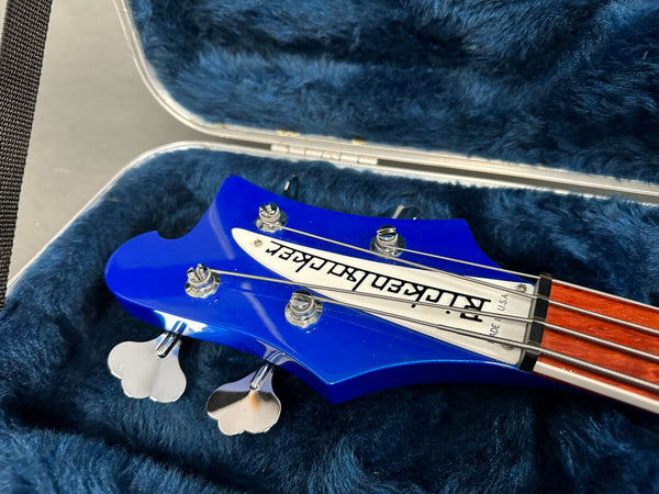 Close-up of blue Rickenbacker bass guitar headstock with tuning pegs and strings inside a plush blue guitar case
