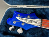 Close-up of blue Rickenbacker bass guitar headstock with tuning pegs and strings inside a plush blue guitar case