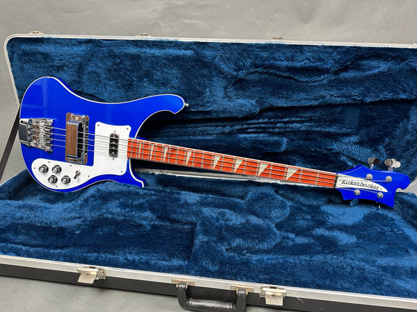 Blue Rickenbacker electric bass guitar with white pickguard and triangular inlays, displayed in blue plush-lined hardshell case