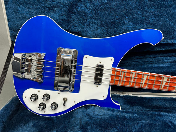 Electric bass guitar with blue body, white pickguard, chrome hardware, and wooden fretboard with rectangular inlays on blue plush background