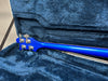 Back of blue electric bass guitar neck and headstock with silver tuning pegs inside blue plush-lined guitar case