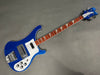 Blue Rickenbacker electric bass guitar with white pickguard and triangular fret inlays on a gray background