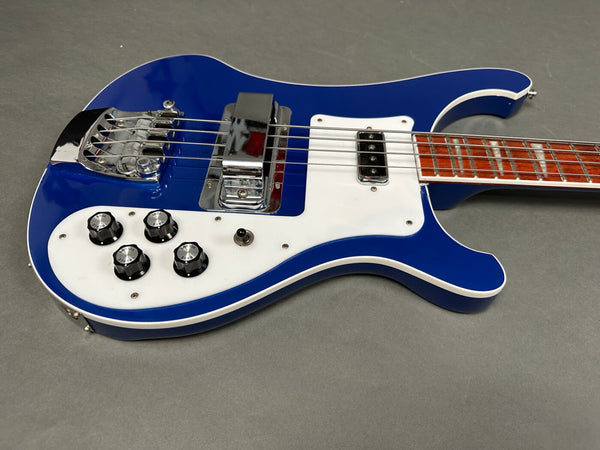 Blue electric bass guitar with white pickguard and chrome hardware on gray background