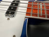 Close-up of electric bass guitar strings, chrome pickup, white pickguard, and rosewood fretboard with inlay, showing wear on blue guitar body edge.