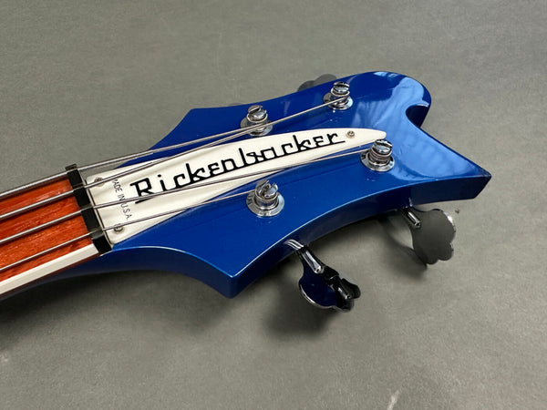 Close-up of blue Rickenbacker bass guitar headstock with chrome tuning pegs and white truss rod cover on gray background