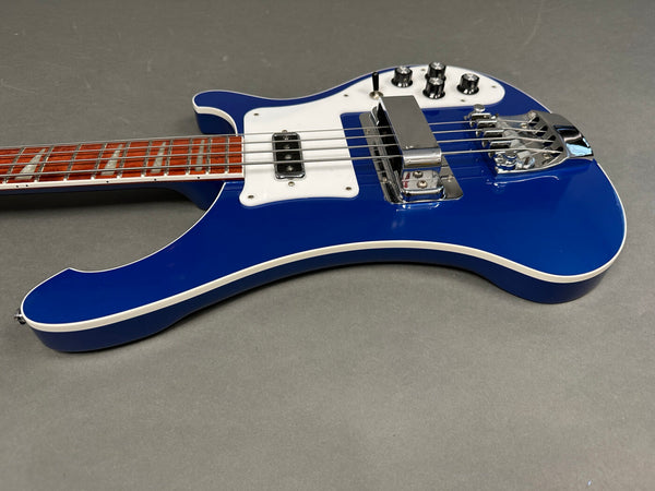 Blue electric bass guitar with white pickguard, chrome hardware, and rosewood fretboard on gray background