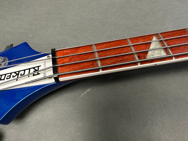 Close-up of blue electric bass guitar neck with wooden fretboard and triangle inlay, featuring metal strings and headstock with "Made in U.S.A." label.