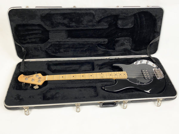 Black electric bass guitar with maple neck and chrome hardware in a black plush-lined hard case on white background