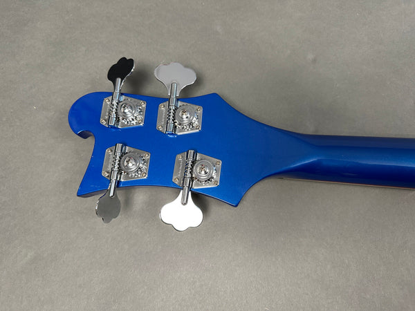Close-up of blue bass guitar headstock with chrome tuning pegs on grey background