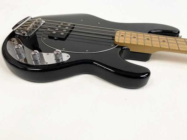 Close-up of black electric bass guitar body with maple neck and chrome control knobs on white background