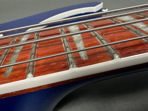 Close-up of bass guitar fretboard with metal frets, steel strings, white binding, and polished wood grain surface