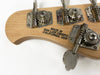 Close-up of bass guitar headstock tuning pegs with "Made in San Luis Obispo California USA" stamped on light wood surface