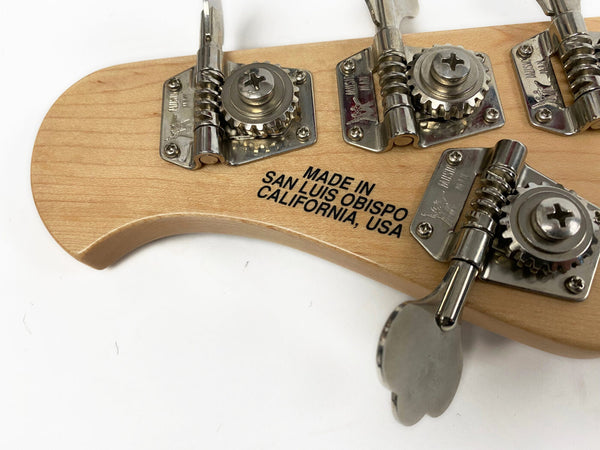 Close-up of bass guitar headstock tuning pegs with "Made in San Luis Obispo California USA" stamped on light wood surface