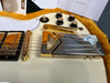 Close-up of white electric guitar bridge and tailpiece with gold hardware, volume and tone control knobs, and toggle switch on guitar body inside a yellow plush-lined case with Gibson dealer tags visible
