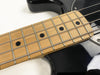 Close-up of maple fretboard with black dot inlays and metal frets on black electric bass guitar body