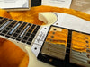 Close-up of a vintage white Gibson Les Paul Custom electric guitar showing the fretboard with block inlays and gold-plated humbucker pickups, resting on a plush orange guitar case interior.