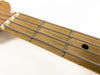 Close-up view of guitar fretboard with metal frets, steel strings, and black dot inlay on light wood neck against white background