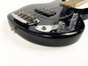 Close-up of black electric bass guitar body showing chrome bridge, control knobs, pickup, and output jack on white background