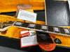 Close-up of Gibson Custom guitar neck and fretboard inside yellow plush-lined hardshell case with Gibson vintage tone circuit card, Certificate of Authenticity, Gibson Custom hang tag, and black Gibson Pure guitar pick.