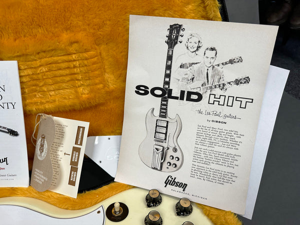 Vintage Gibson Les Paul guitar promotional flyer titled "Solid Hit" with guitar illustration and text description, placed inside guitar case with Gibson tags and white electric guitar body and control knobs visible