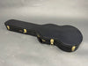 Black hard shell guitar case with gold latches and handle, shaped for acoustic guitars, on gray background