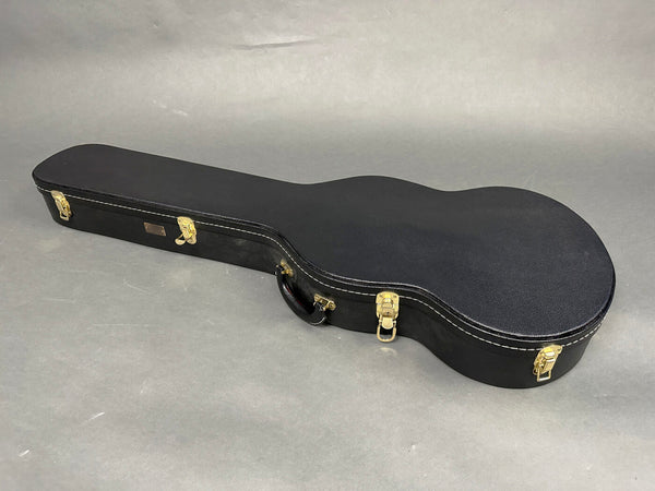 Black hard shell guitar case with gold latches and handle, shaped for acoustic guitars, on gray background