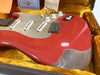 Close-up of vintage Fender Stratocaster electric guitar with worn red finish and silver pickguard in yellow lined case