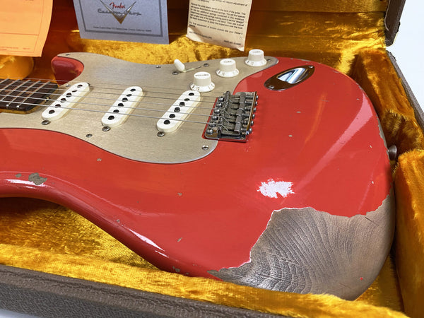 Close-up of vintage Fender Stratocaster electric guitar with worn red finish and silver pickguard in yellow lined case