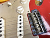 Close-up of vintage Fender electric guitar bridge, pickups, and volume knob on red and silver guitar body with metal hardware and six strings.