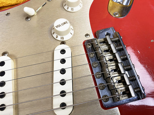 Close-up of vintage Fender electric guitar bridge, pickups, and volume knob on red and silver guitar body with metal hardware and six strings.