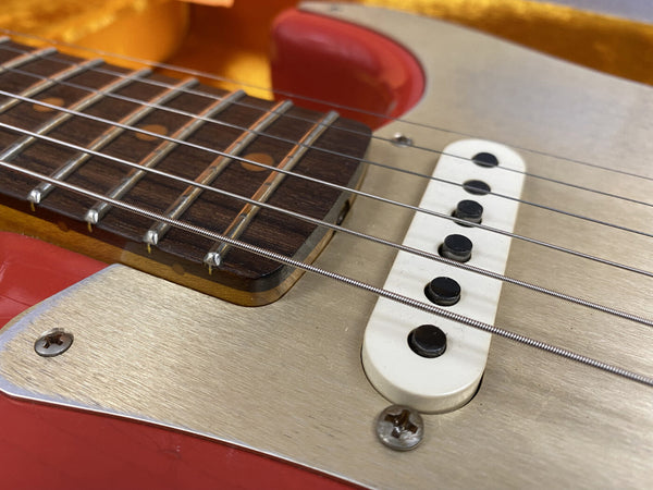 Close-up of electric guitar bridge and strings with metal pickguard and rosewood fretboard on red body