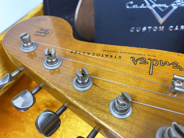 Close-up of Fender Stratocaster guitar headstock with tuning pegs and strings in vintage yellow finish inside a guitar case