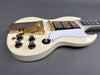 White electric guitar with gold hardware, white pickguard, black control knobs, and three gold pickups on gray background