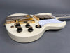 Close-up of white electric guitar body with gold hardware, black control knobs, and white pickguard on gray background