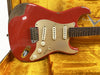 Vintage red Fender Stratocaster electric guitar with aged gold pickguard and three single-coil pickups displayed in a yellow velvet Fender Custom Shop guitar case