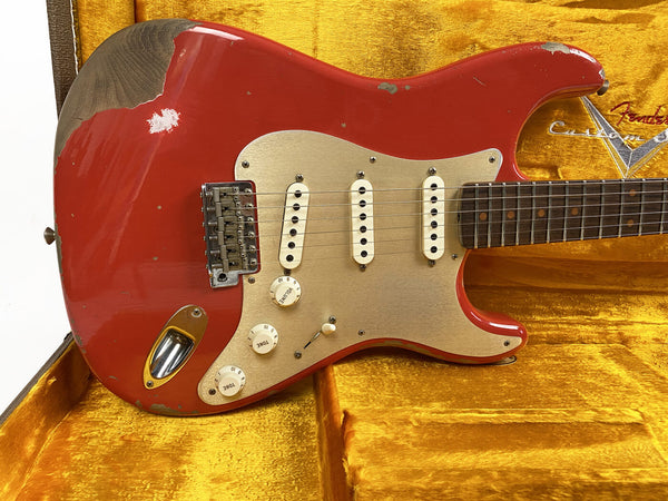 Vintage red Fender Stratocaster electric guitar with aged gold pickguard and three single-coil pickups displayed in a yellow velvet Fender Custom Shop guitar case