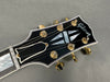Close-up of Gibson guitar headstock with mother-of-pearl inlay and gold tuning pegs on gray background