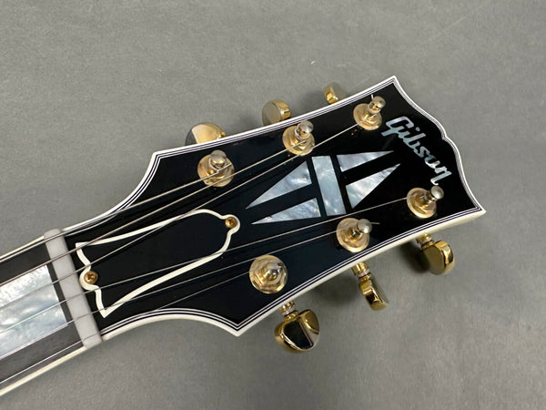 Close-up of Gibson guitar headstock with mother-of-pearl inlay and gold tuning pegs on gray background