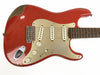 Vintage red electric guitar with worn paint and cream pickguard, three single-coil pickups, and rosewood fretboard on white background