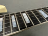 Close-up of electric guitar fretboard with mother-of-pearl block inlays and metal frets, six steel strings, and cream binding on a dark wood fingerboard.