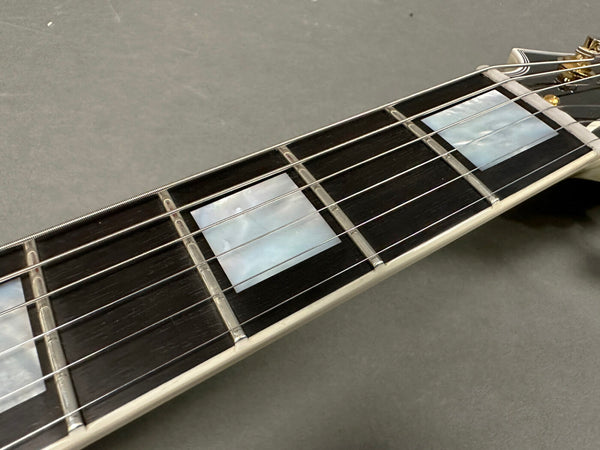Close-up view of guitar fretboard with mother-of-pearl block inlays and steel strings on dark wood fingerboard